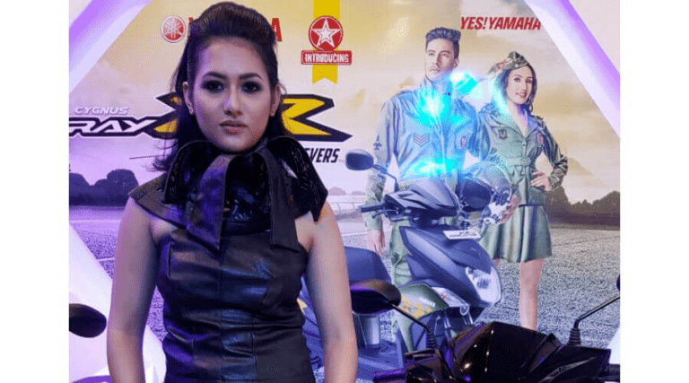 A person posing in front of a promotional backdrop featuring a scooter and graphic silhouettes of a man and woman.