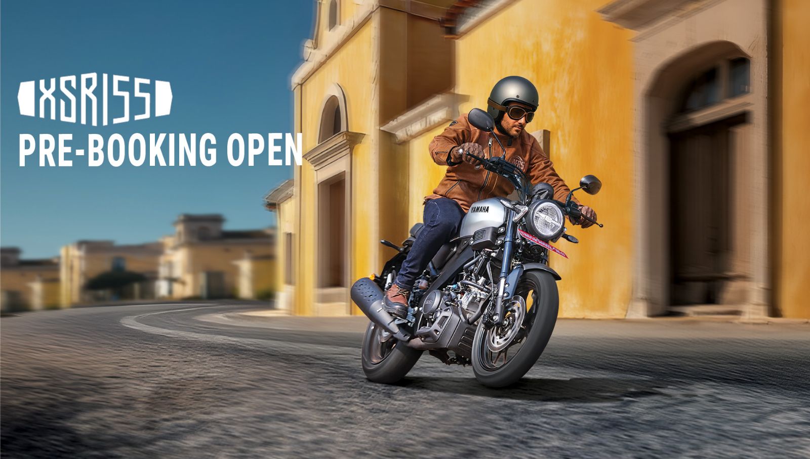 A rider operates a Yamaha XSR155 motorcycle on a sunlit urban street beside historic ochre buildings with pre-booking text.